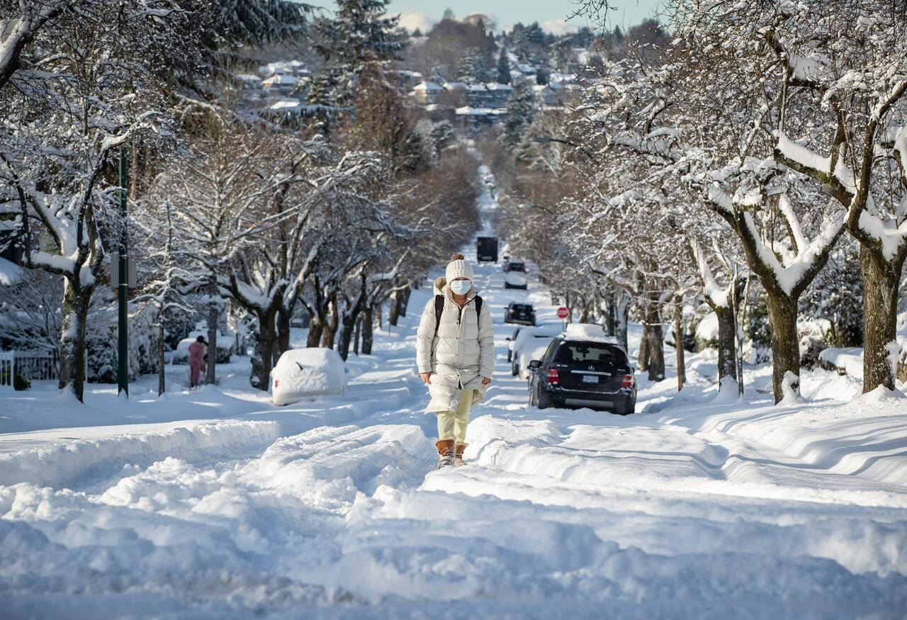 A woman bundled up for the cold weather walks up a snow-covered street in Vancouver, on Thursday, December 30, 2021. THE CANADIAN PRESS/Darryl Dyck