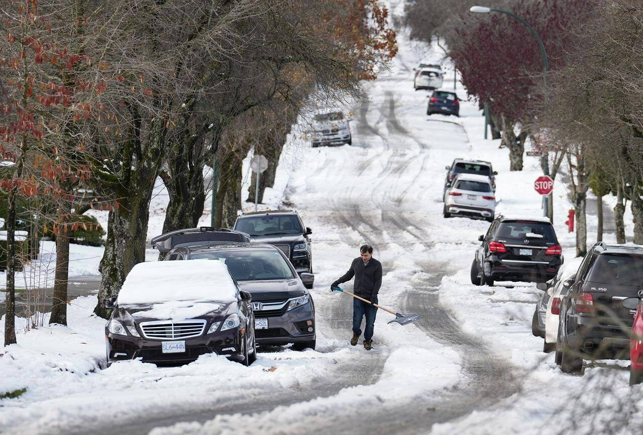A man pauses while digging out snow from under a car stuck on a street in the aftermath of a snowstorm, in Vancouver, on Wednesday, Nov. 30, 2022. THE CANADIAN PRESS/Darryl Dyck