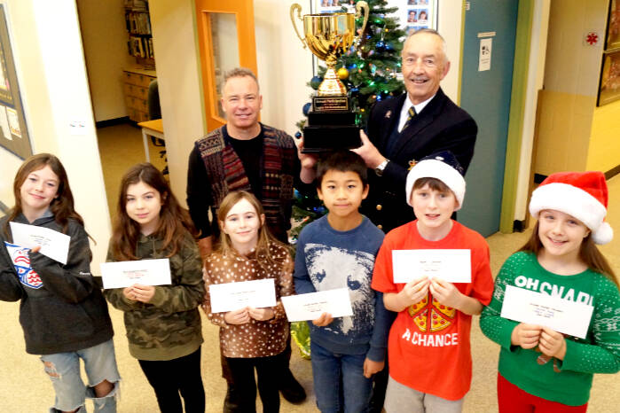 John Muir Elementary School students Kahlan Thornton (left), Callie Watson, Sophia Smith, Konnor May, Weston Cole, and Carly Clare hold up envelopes with their prizes for the Sooke Legion’s Remembrance Day Poster and Literary Contest. School principal John Muir and Legion member Ken Levert stand behind the students with the trophy that goes to the school with the highest percentage of participation in the contest. (Rick Stiebel - Sooke News Mirror)