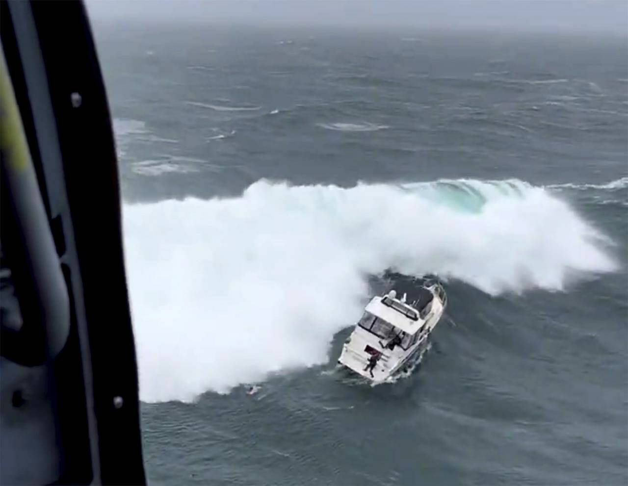 In this photo provided by the U.S. Coast Guard Pacific Northwest, a Coast Guard rescue swimmer reaches a boat right before a giant wave rolled the craft at the mouth of the Columbia River in Oregon on Friday, Feb. 3, 2023. The newly minted Coast Guard rescue swimmer saved the life of a man who was piloting the yacht. (AET1 Kyle Turcotte/U.S Coast Guard Pacific Northwest via AP)