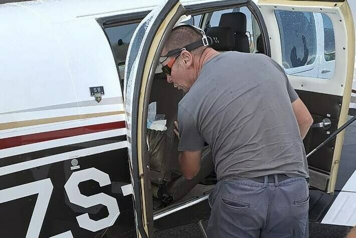 In this photo provided by Brian Emmenis, fire officer and snake handler Johan de Klerk looks inside a plane, in Welkom, South Africa, as he searches for a venomous snake that the pilot found hiding under his seat midair, Monday April 3, 2023. Rudolf Erasmus had four passengers on board the light aircraft during Monday's flight when he felt “something cold” slide across his lower back. He glanced down to see the head of a fairly large Cape Cobra “receding back under the seat,” he said. (Brian Emmenis via AP)