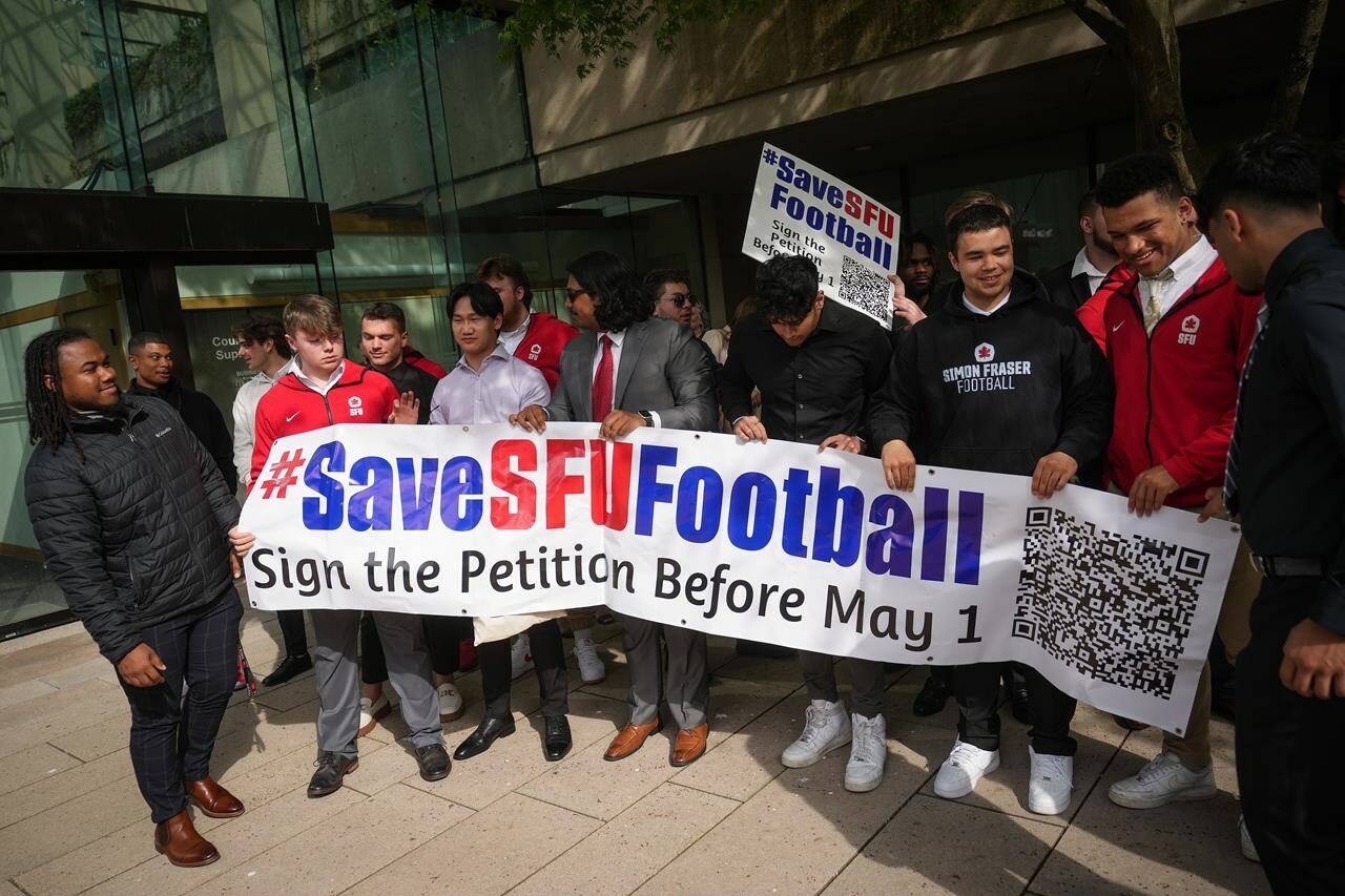 Simon Fraser University football team players hold a banner after attending a hearing at B.C. Supreme Court, in Vancouver, on Monday, May 1, 2023.The Simon Fraser Football Alumni Society outlined details Friday of a proposal it sent to the school regarding the future of its football program.THE CANADIAN PRESS/Darryl Dyck