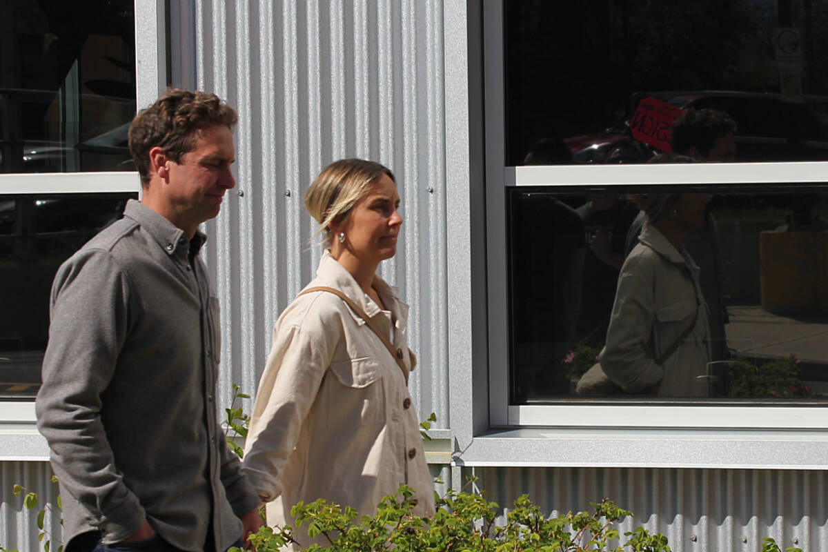 Coun. David Frisch and his wife Chantal enter the Comox Valley Regional District headquarters. A group of protesters stands by, with placards calling for his resignation. (Connor McDowell/Comox Valley Record)