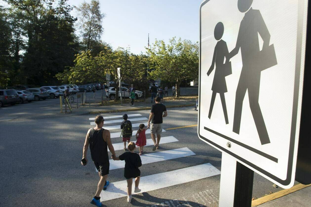 Children walk with their parents to a school in North Vancouver on Sept. 10, 2020. All students from kindergarten to Grade 9 in British Columbia public schools will now be assessed with a proficiency scale instead of letter grades. THE CANADIAN PRESS/Jonathan Hayward