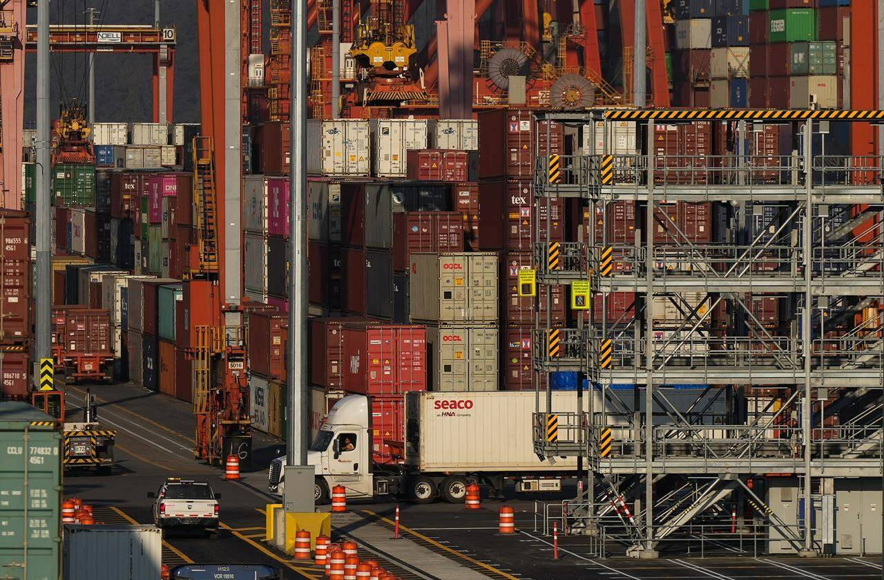 A truck carries a cargo container at the Port of Vancouver Centerm container terminal as others are stacked under gantry cranes, in Vancouver, on Friday, Oct. 14, 2022. The Canadian Chamber of Commerce says it is “deeply disturbed” by the strike notice the union for British Columbia’s port workers’ made that said its members were prepared to walk out on Saturday. THE CANADIAN PRESS/Darryl Dyck