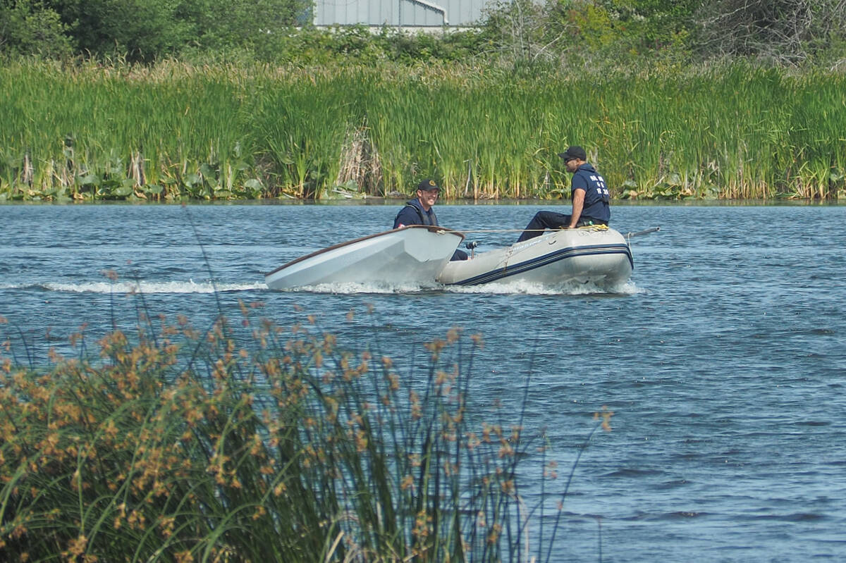 Nanaimo Fire Rescue firefighters bring a small sailing dinghy ashore after retrieving its occupants from Diver Lake after the craft capsized Tuesday, July 4. (Chris Bush/News Bulletin)