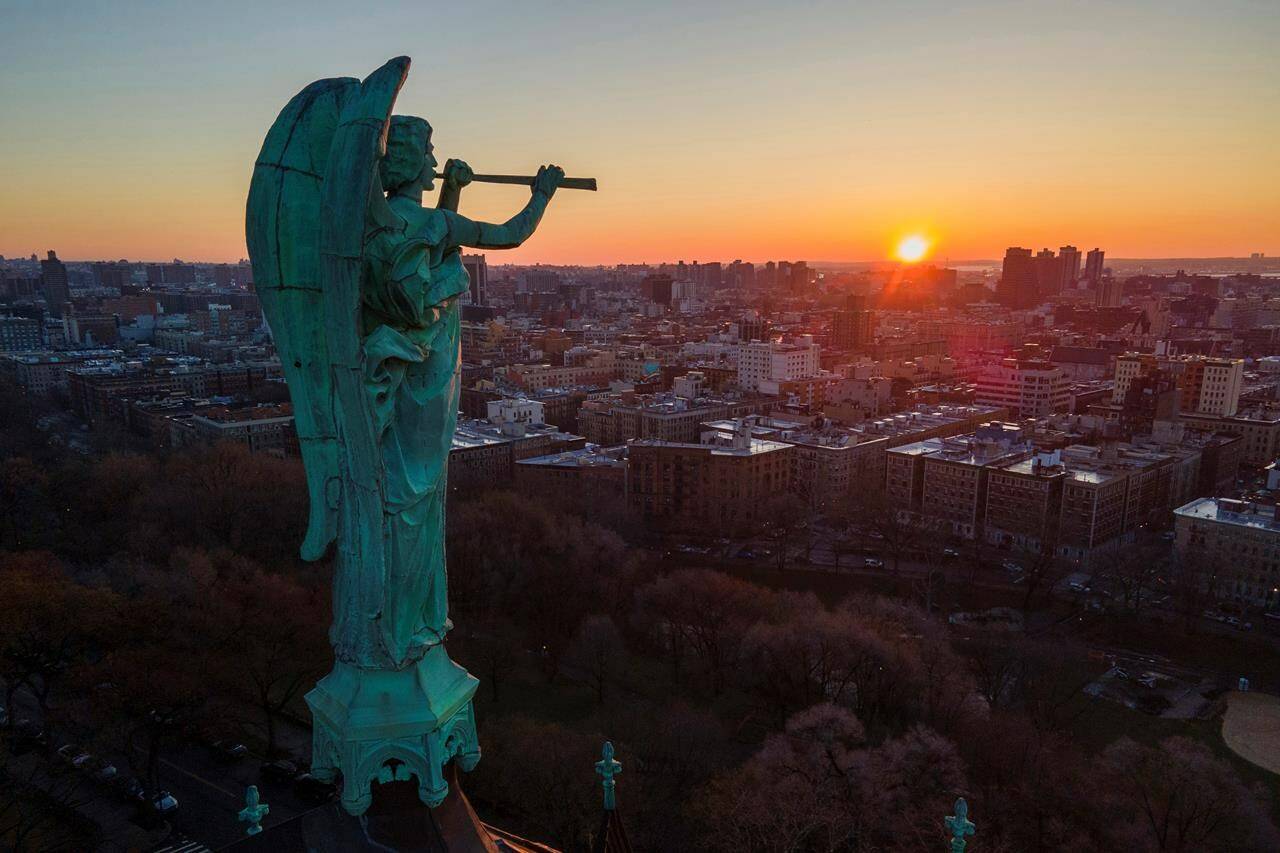 FILE - A bronze statue of the Archangel Gabriel blowing a trumpet stands at the Cathedral of St. John the Divine as the sun rises in the Morningside Heights neighborhood of the borough of Manhattan in New York on Sunday, March 26, 2023. (AP Photo/Ted Shaffrey, File)