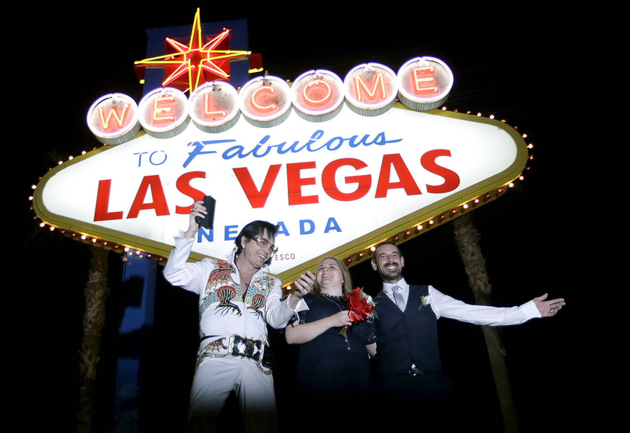 Elvis tribute artist Eddie Powers poses for a photo with newlyweds Rob and Kelly Roznowski after he married them at the Welcome to Las Vegas sign in Las Vegas. (Black Press Media File Photo)