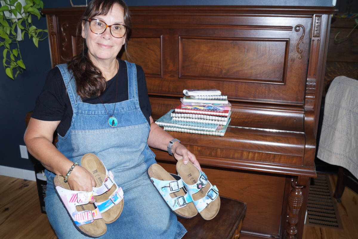 Long-time Sooke resident Doreen Carscadden, shown here with a few of 36 books of art she’s catalogued and the sandals chosen for an exclusive run of two pairs of Birkenstock sandals. (Rick Stiebel - Sooke News Mirror)