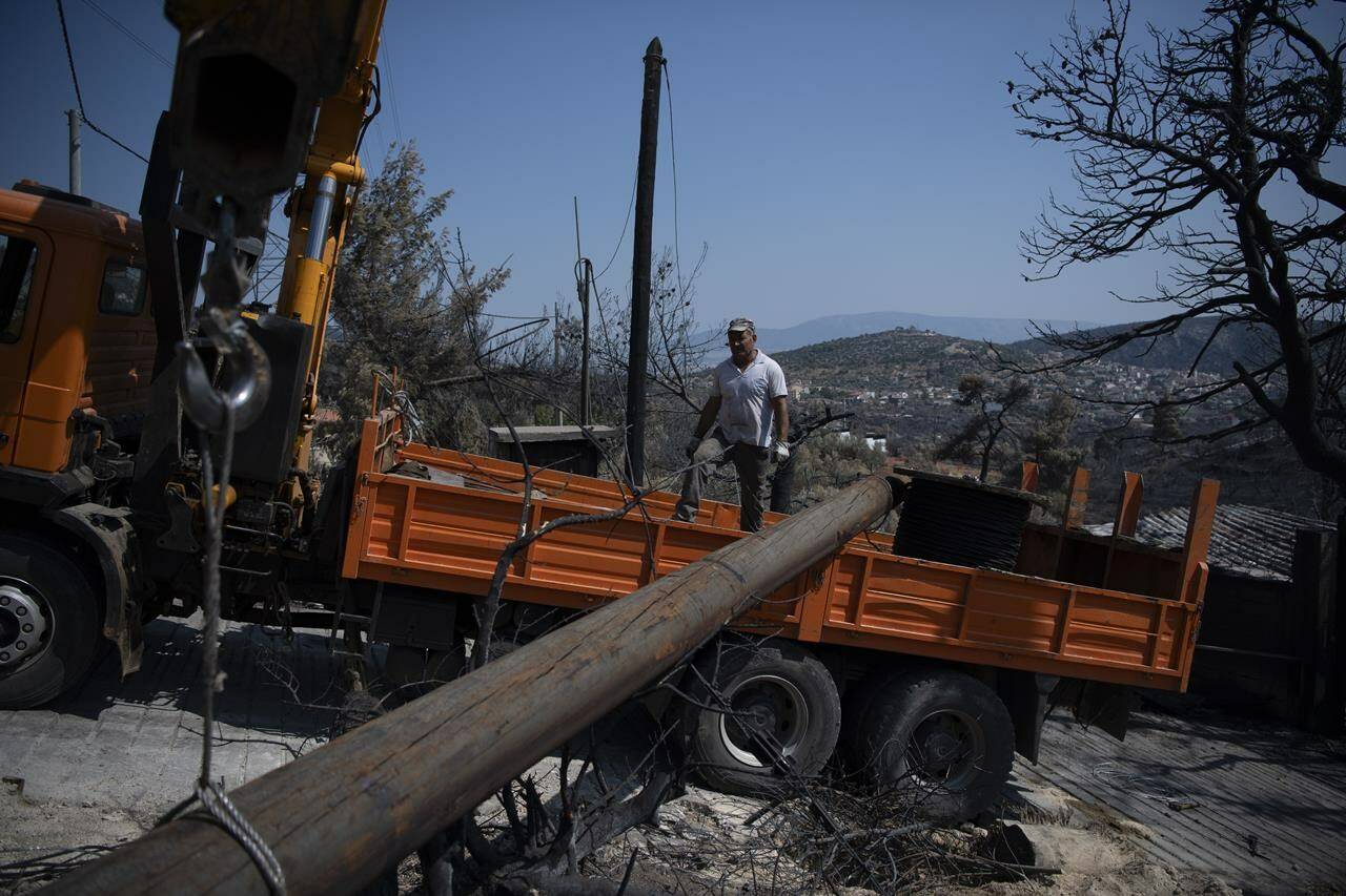 Workers of the electric company replace a utility pole after a wildfire in the Fyli suburb, northwest Athens, Greece, Friday, Aug. 25, 2023. Authorities battling a major wildfire in northeastern Greece that has been described as the European Union’s largest single fire recorded have recovered another body, the fire department says, bringing the total death toll of wildfires in Greece this week to 21. (AP Photo/Michael Varaklas)