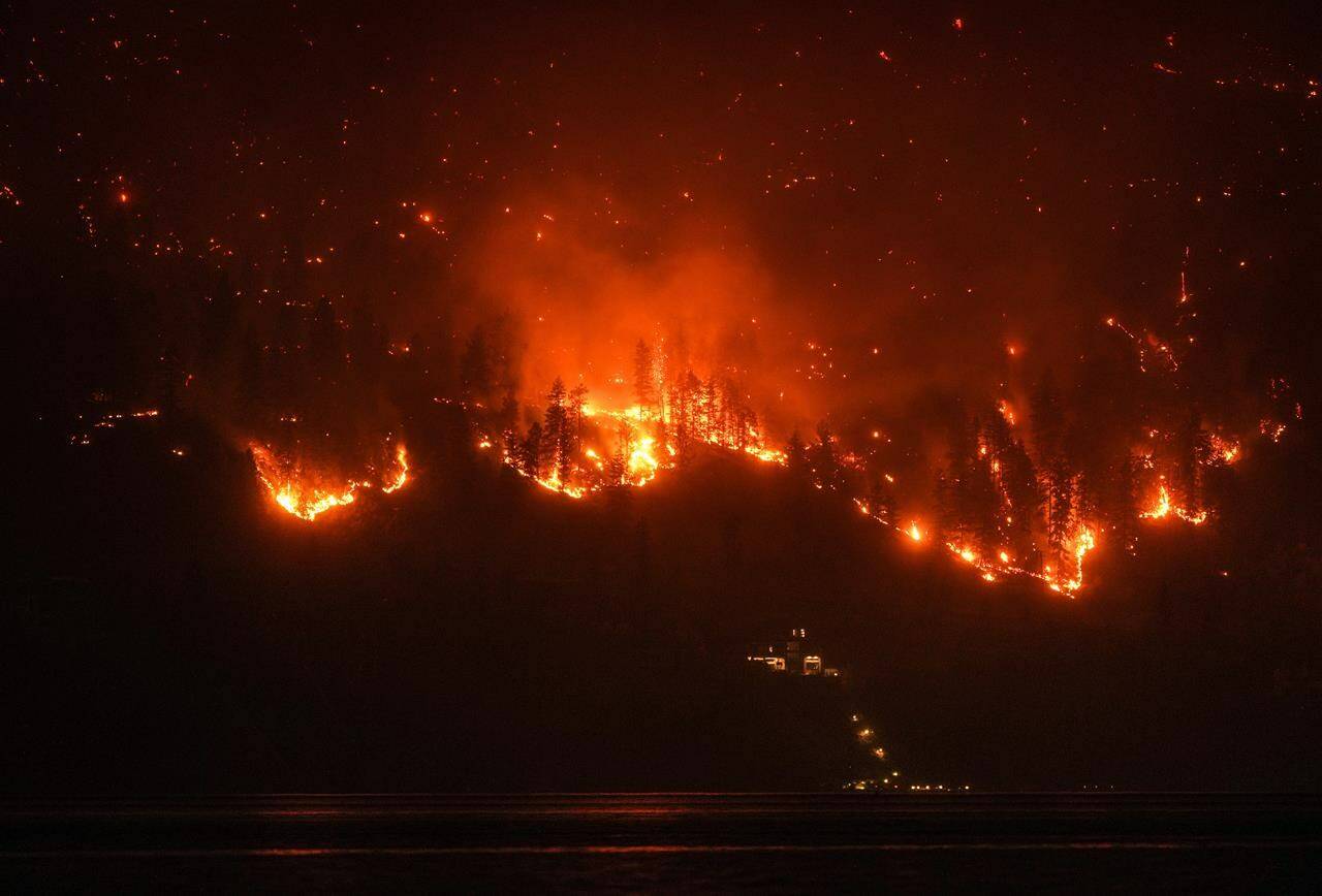 The McDougall Creek wildfire burns on the mountainside above a lakefront home in West Kelowna on Aug. 18. THE CANADIAN PRESS/Darryl Dyck