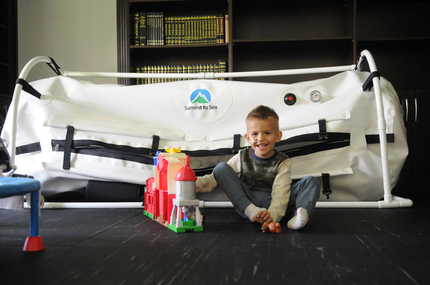 Three-year-old Ryah Hope plays in his Yarrow home on Oct. 13, 2023. Behind him is an in-home hyperbaric oxygen therapy chamber. (Jenna Hauck/ Chilliwack Progress)