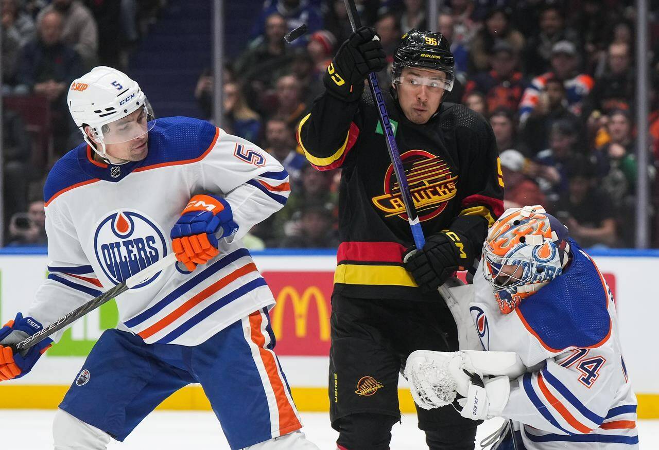 Vancouver Canucks’ Andrei Kuzmenko, centre, and Edmonton Oilers’ Cody Ceci, left, watch the puck after it deflected off the mask of Edmonton goalie Stuart Skinner during the second period of an NHL hockey game in Vancouver, on Monday, Nov. 6, 2023. THE CANADIAN PRESS/Darryl Dyck