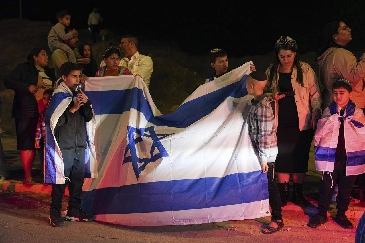People wait for the convoy carrying newly released hostages from the Gaza Strip, in Ofakim, Israel on Sunday, Nov. 26, 2023. (AP Photo/Tsafrir Abayov)