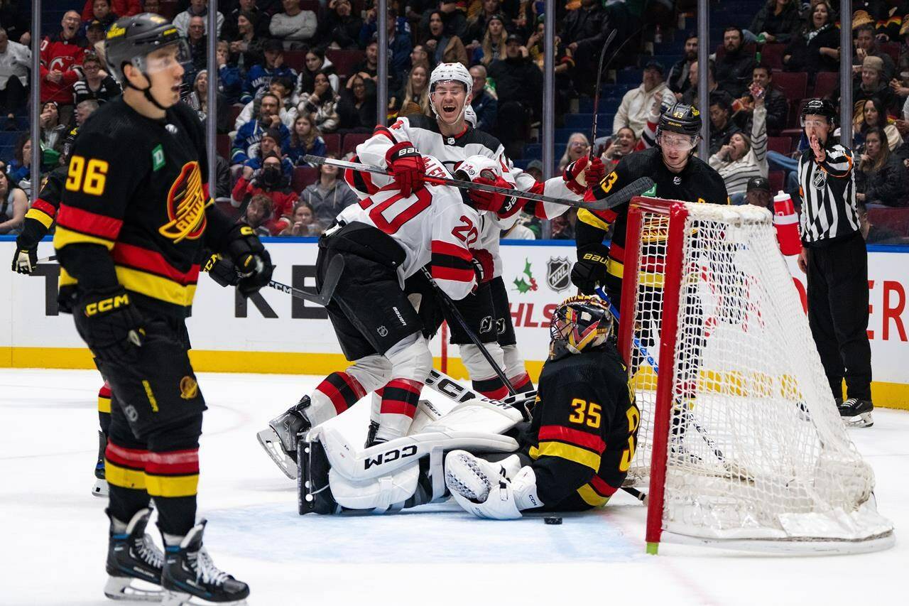 New Jersey Devils’ Nathan Bastian (14) and Michael McLeod (20) celebrate McLeod’s goal on Vancouver Canucks goaltender Thatcher Demko (35) as Vancouver’s Quinn Hughes (43) watches during the first period of an NHL hockey game in Vancouver on Tuesday, Dec. 5, 2023. THE CANADIAN PRESS/Ethan Cairns