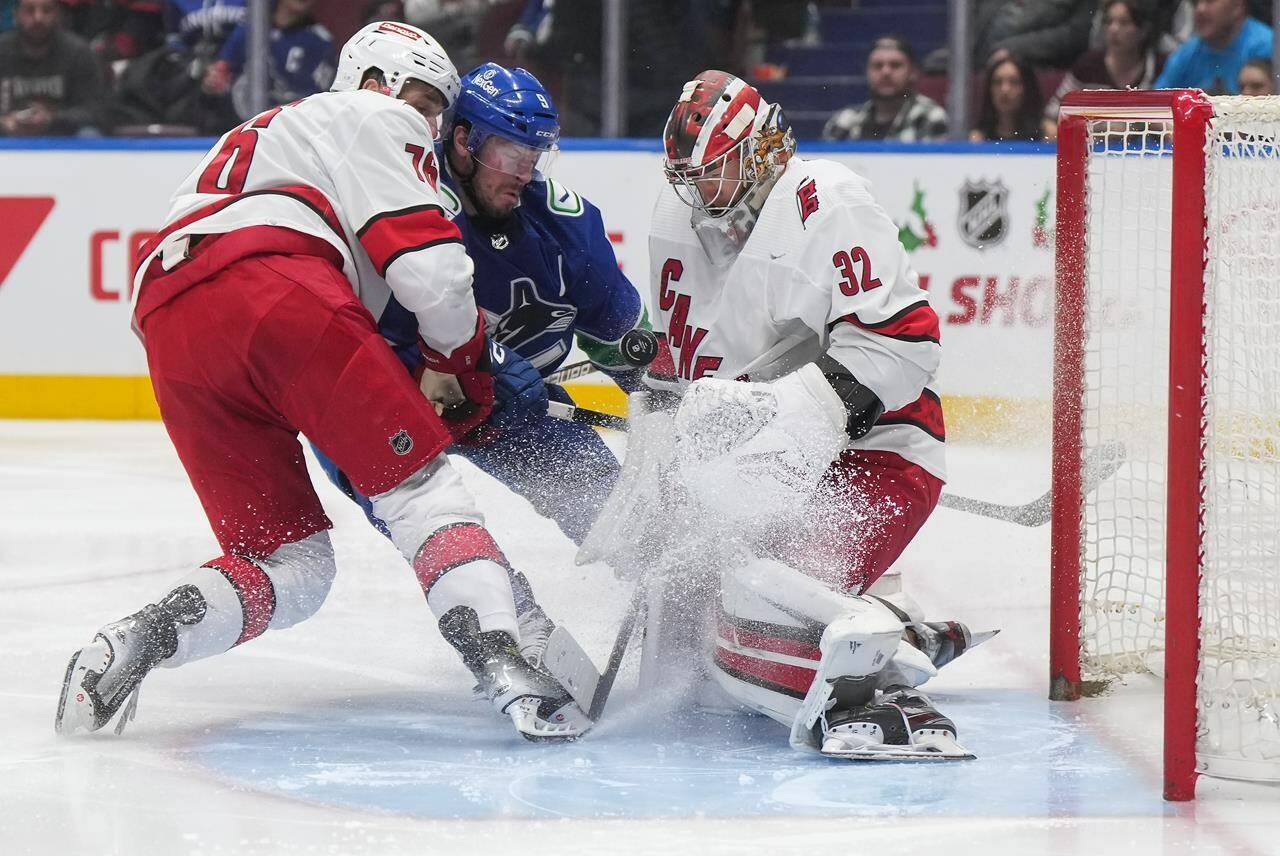 Carolina Hurricanes goalie Antti Raanta (32) makes the save as Brady Skjei, left, checks Vancouver Canucks’ J.T. Miller during the second period of an NHL hockey game in Vancouver, on Saturday, Dec. 9, 2023. THE CANADIAN PRESS/Darryl Dyck