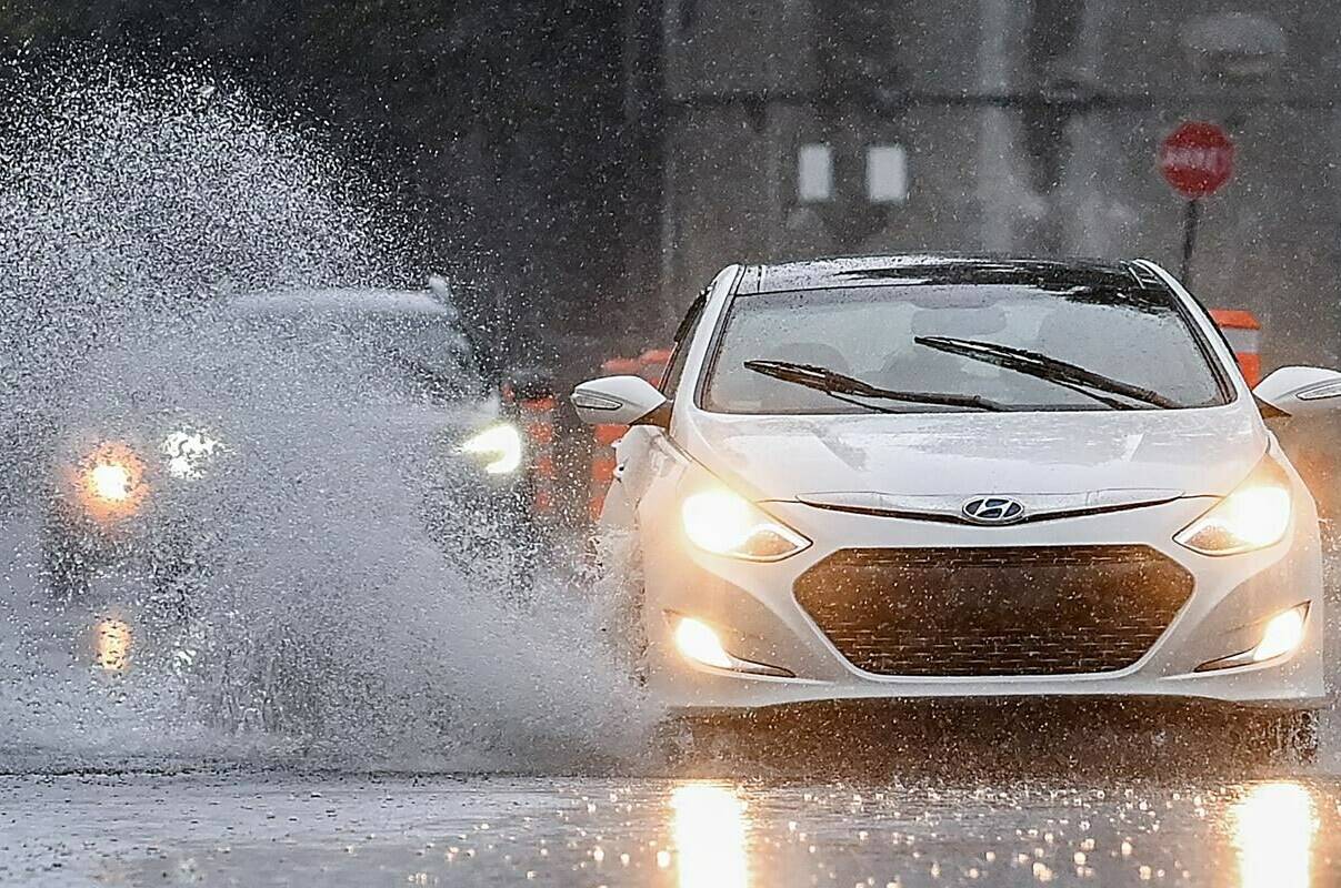 As high inflation eats away the revenues of cities and towns, communities are increasingly being battered by historic fires, flooding, heat and ice storms, and having to dispense additional sums to guard against severe weather and clean up in its aftermath. A motorist makes their way along a street through pooling water during heavy rain in Montreal, Saturday, Oct. 7, 2023.THE CANADIAN PRESS/Graham Hughes