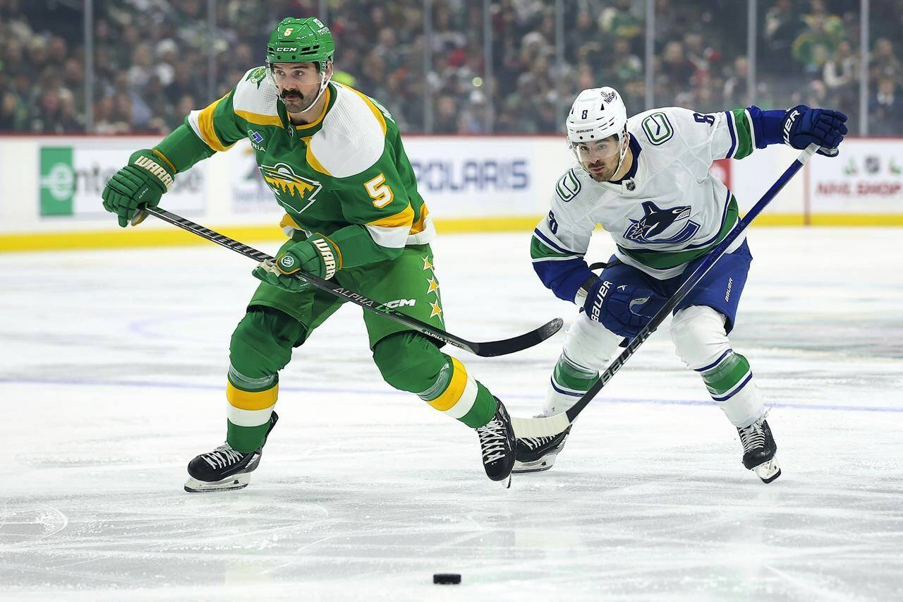 Minnesota Wild defenceman Jake Middleton (5) and Vancouver Canucks right wing Conor Garland (8) compete for the puck during the first period of an NHL hockey game Saturday, Dec. 16, 2023, in St Paul, Minn. (AP Photo/Matt Krohn)