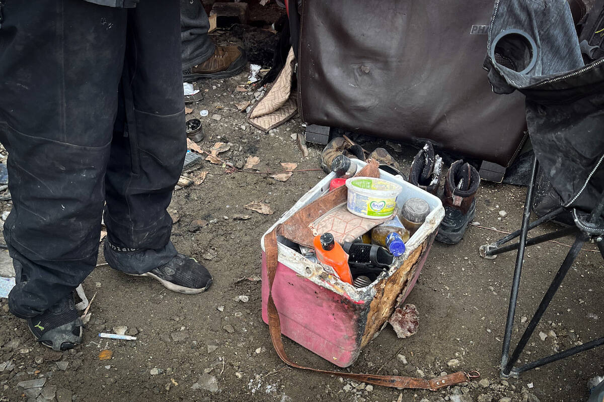 A Kelowna Tent City resident pictured with his burnt cooler after a fire spread from a neighbouring tent. (Jacqueline Gelineau/Capital News)